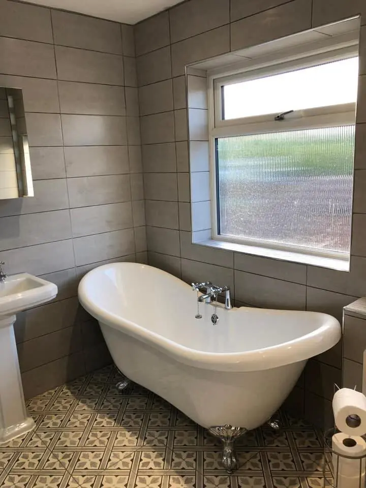 The same bathroom finished, with a roll top bath, tiled walls and a patterned floor