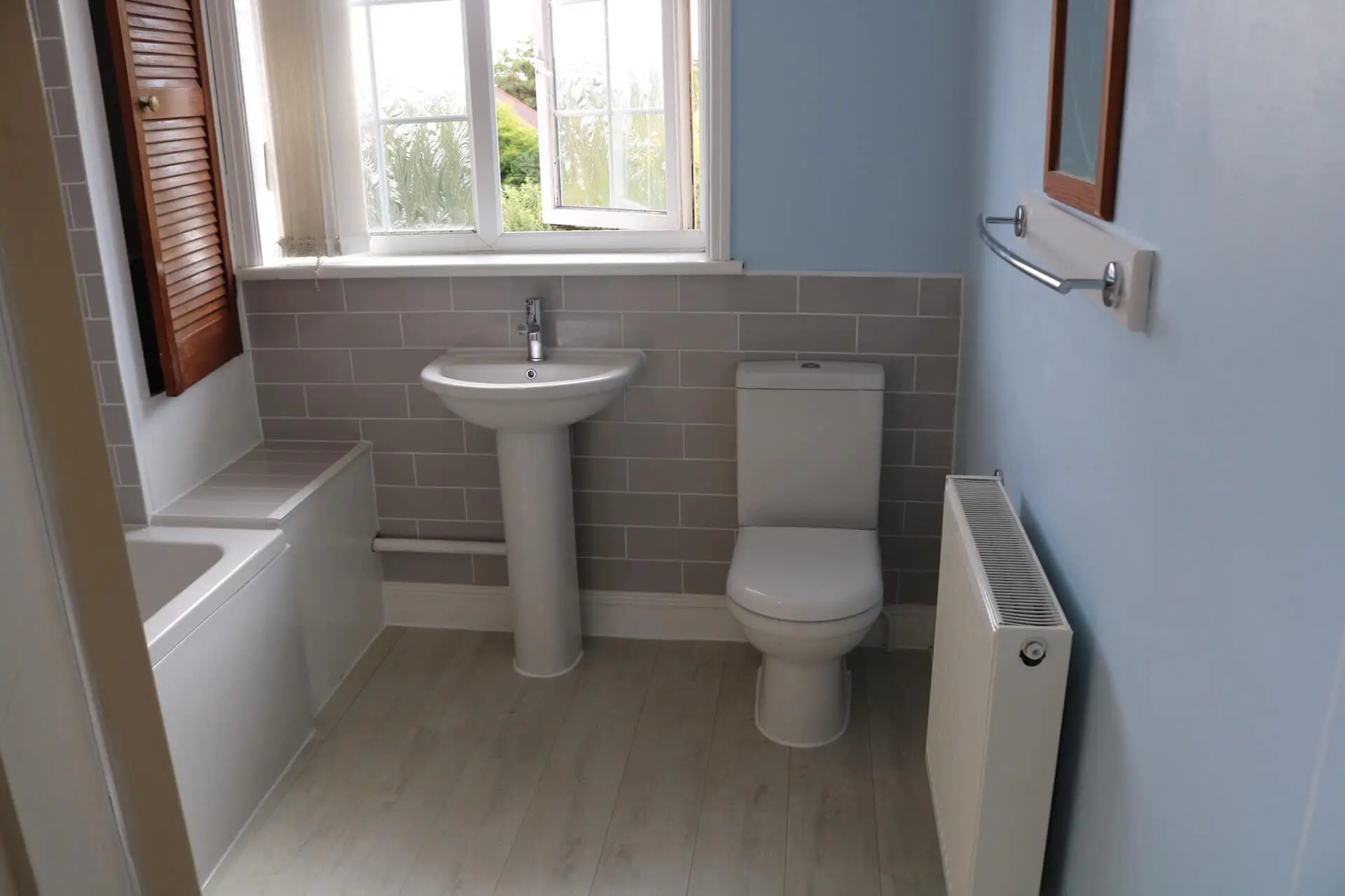 A bathroom with a pedestal basin, a white toilet, a panel radiator and a bath, with pale blue walls