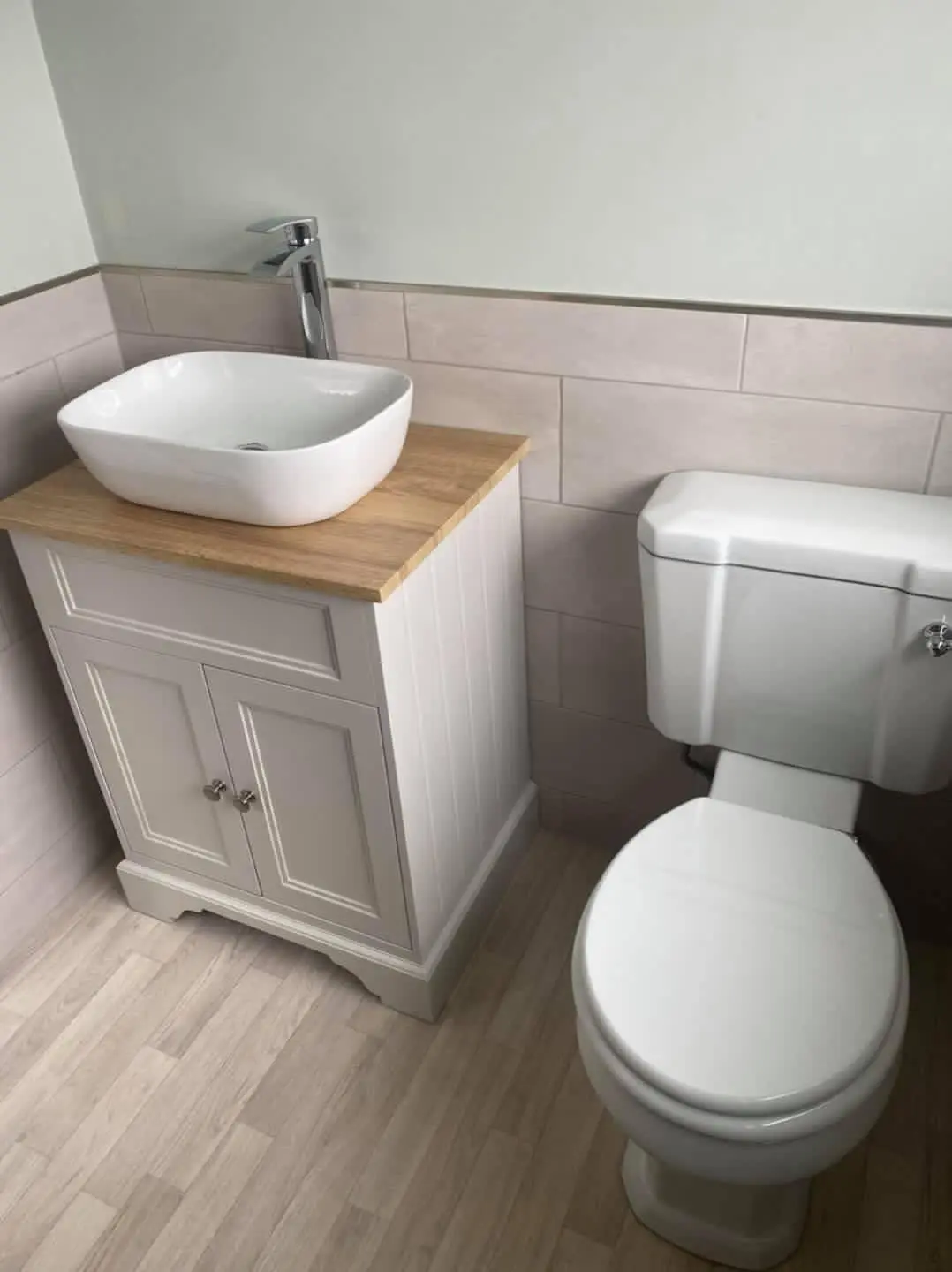 A basin with a chrome tap on a wooden topped vanity unit beside a white toilet