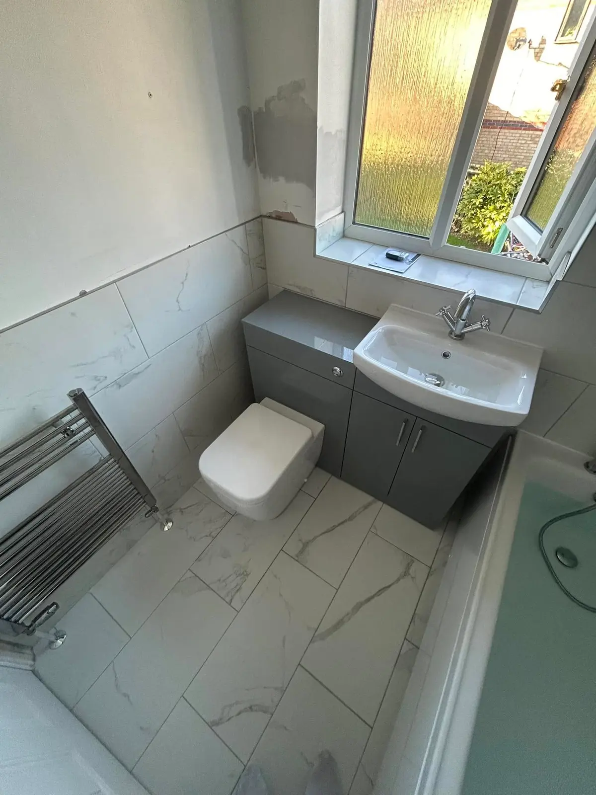 A bathroom with marble effect floor tiles, a grey vanity unit with a basin, a white toilet and a heated towel rail