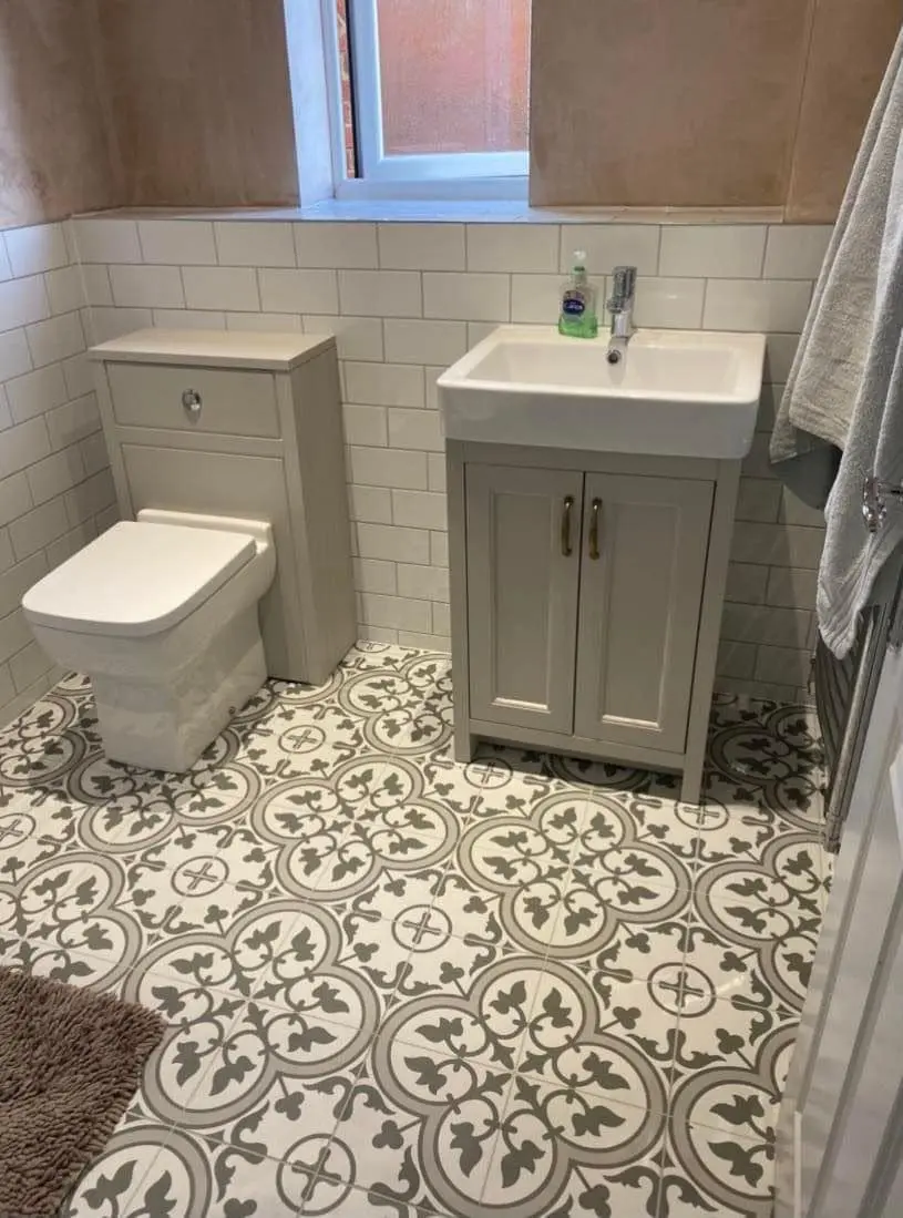 A grey vanity unit and white toilet on a patterned tile floor, with white metro tiles behind