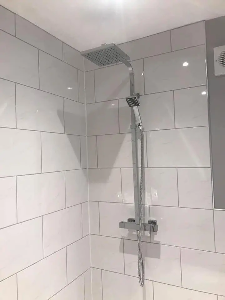 A square rain shower head on a chrome bar against large white tiles